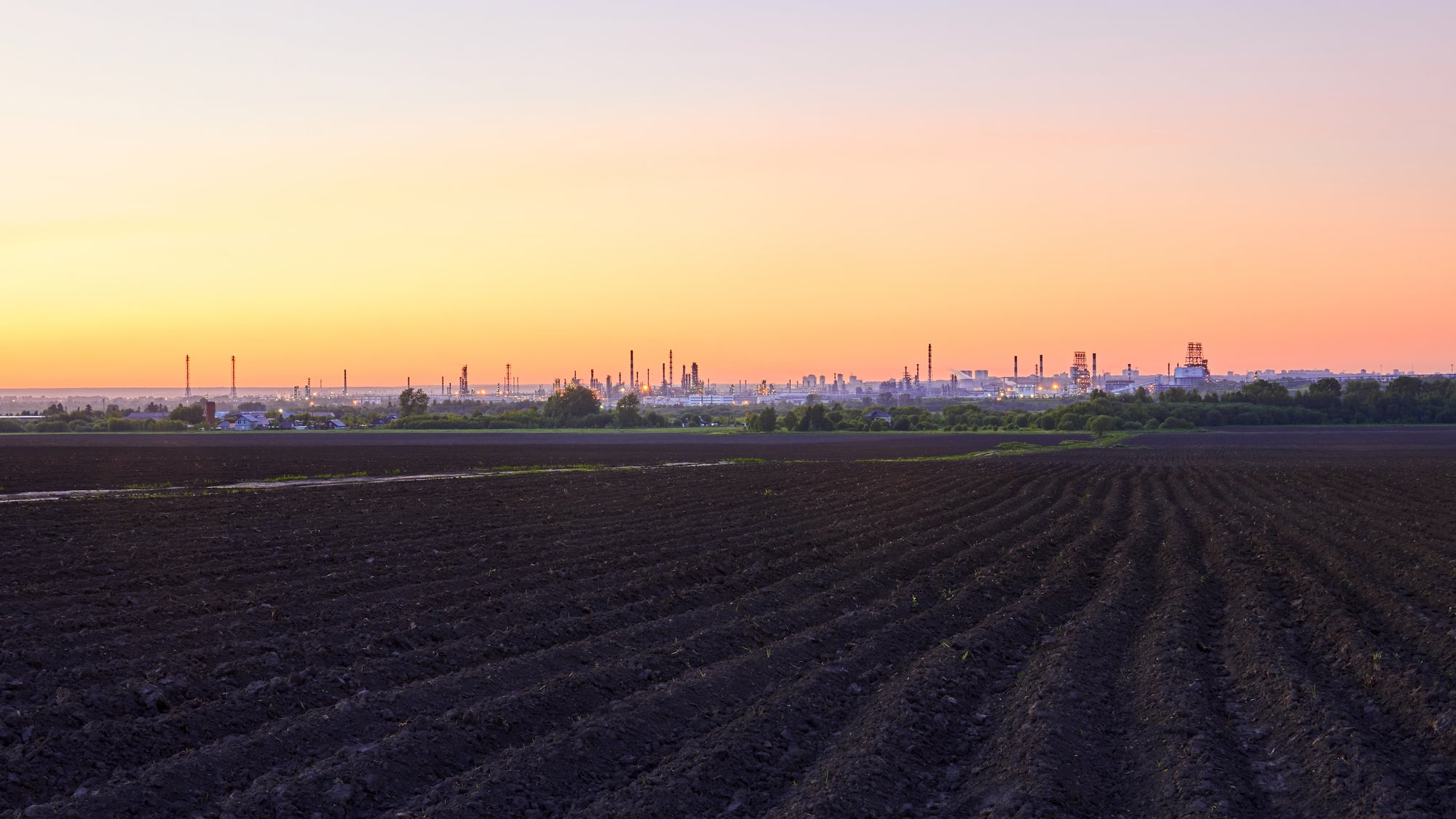 evening rural landscape with plowed fields and a huge oil refinery on the horizon