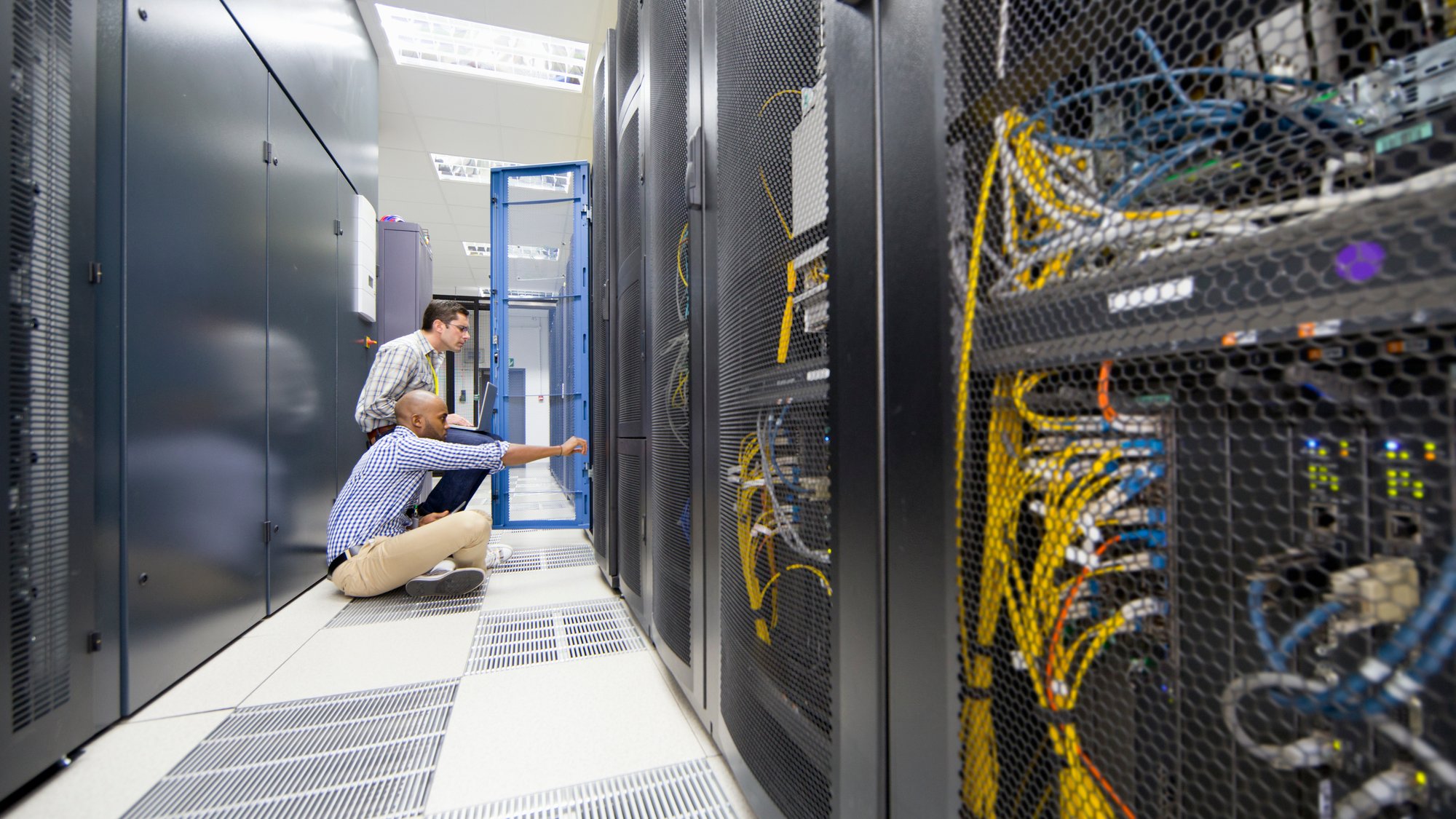 Technicians checking server in the data center hall using a laptop and a digital tablet